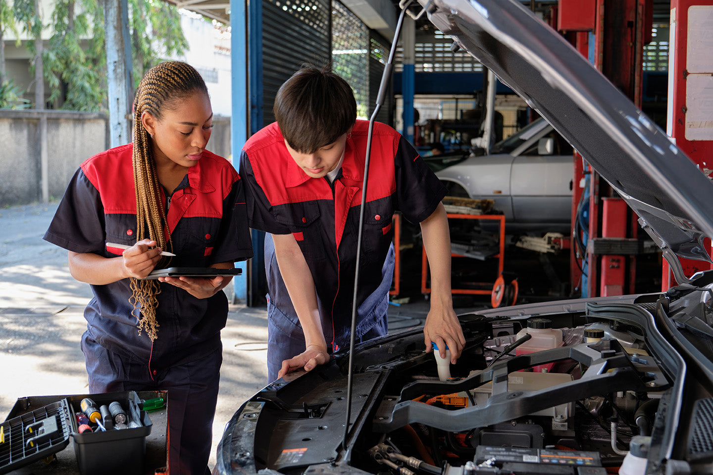 Two mechanics inspecting a car engine in an auto repair shop